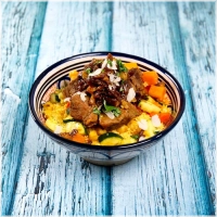 Gestoomde glutenvrije couscous met zacht gegaard rundvlees in geurige bouillon. Klassieke groenten zoals courgette, pompoen, zoete aardappel, wortel, witte kool, kikkererwten, seizoengroenten, gekarameliseerde ui en rozijnen<br><br>